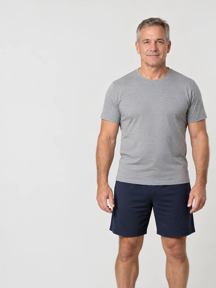 Man van middelbare leeftijd met een atletische lichaamsbouw, staand in grijs T-shirt en donkere short